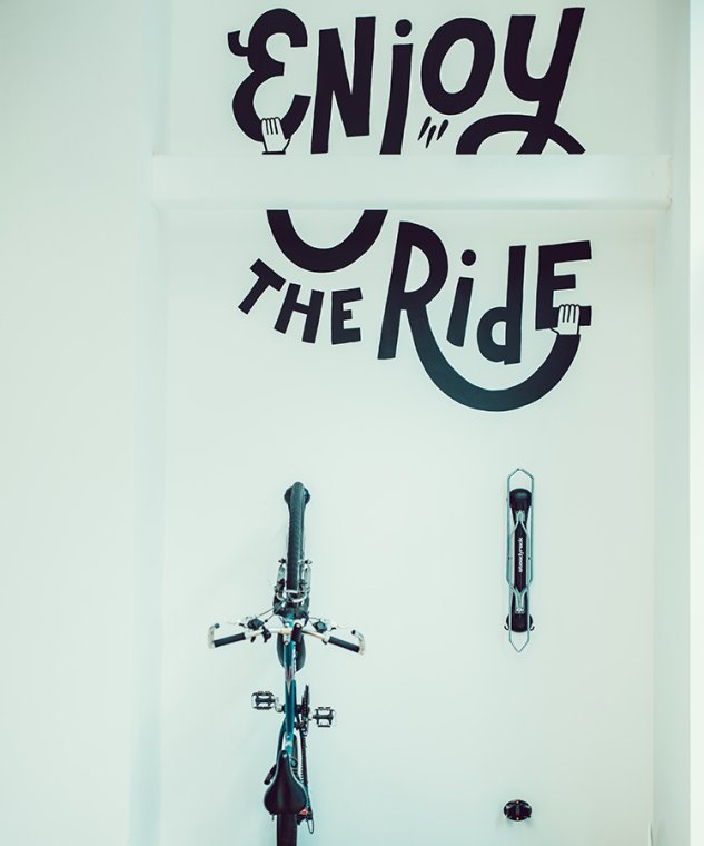 Mural on the wall shows "Enjoy the ride". Below it is storage for two bicycles. 