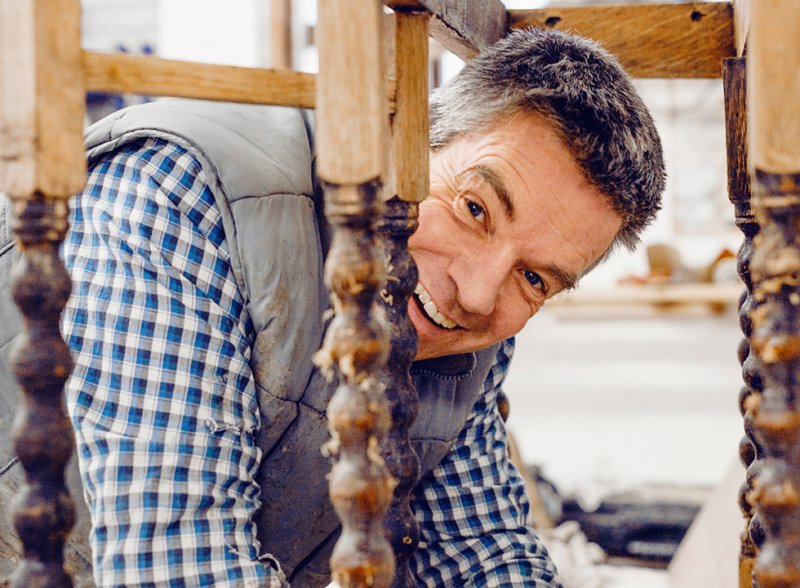 A Betel-trained furniture restorer peering round a turned table leg and looking into the camera